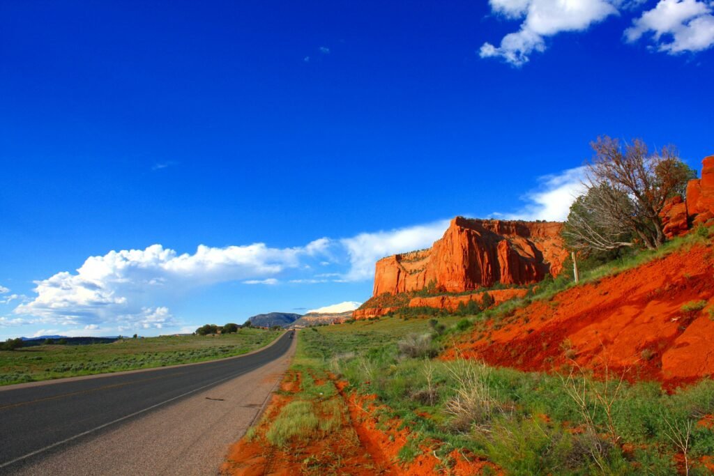 Vibrant red rock formations next to an open road under a clear blue sky, perfect for travel inspiration.