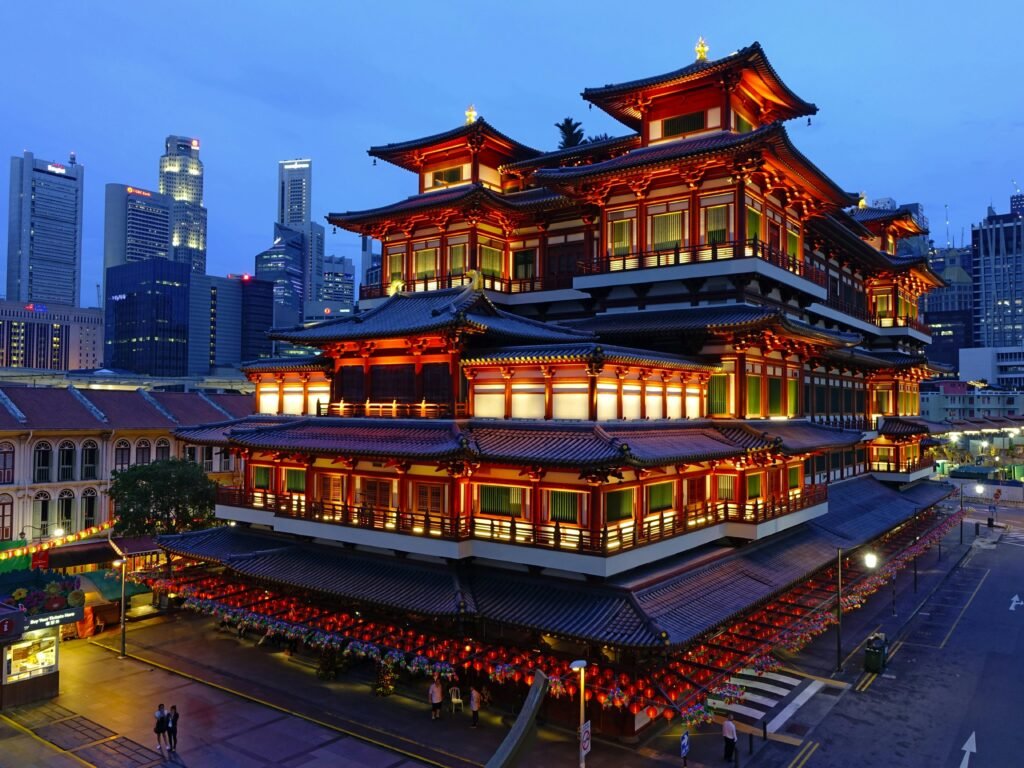 Illuminated Buddha Tooth Relic Temple in Singapore's Chinatown, city skyline in the background.